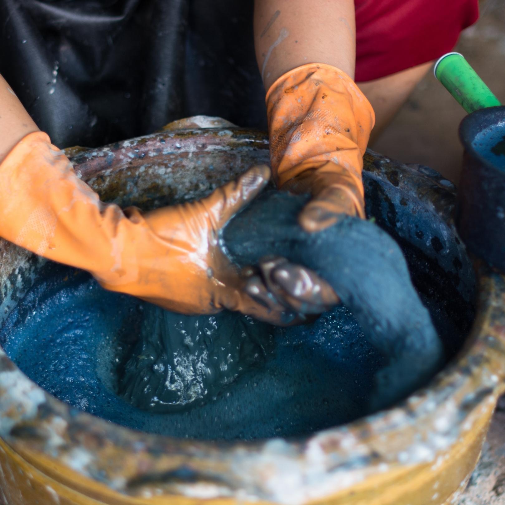 image of hands wearing orange gloves ringing a cloth in a tub filled with indigo dye.